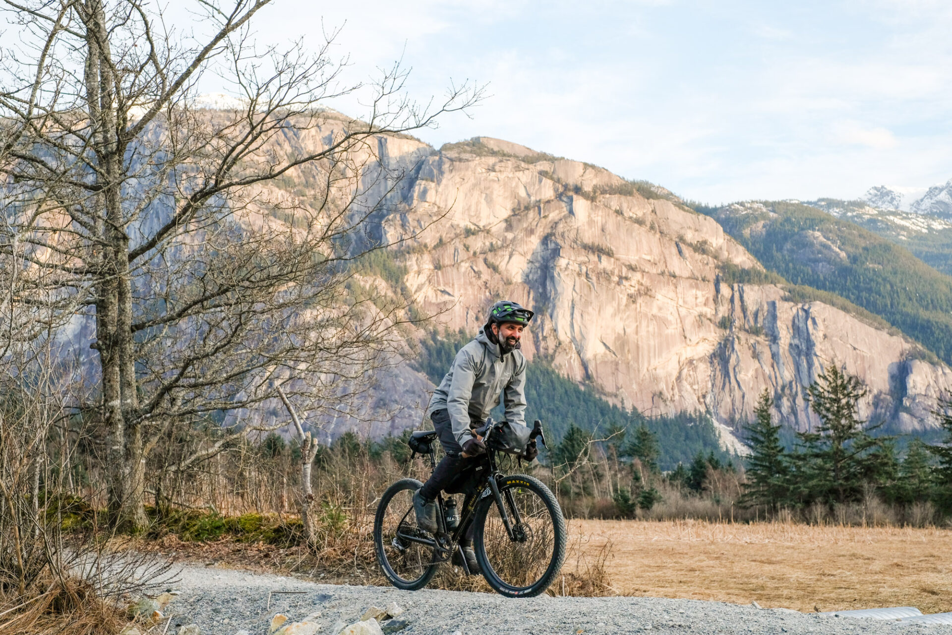 A man rides his bicycle on a rural path in Squamish with the Stawamus Chief mountain in the background.