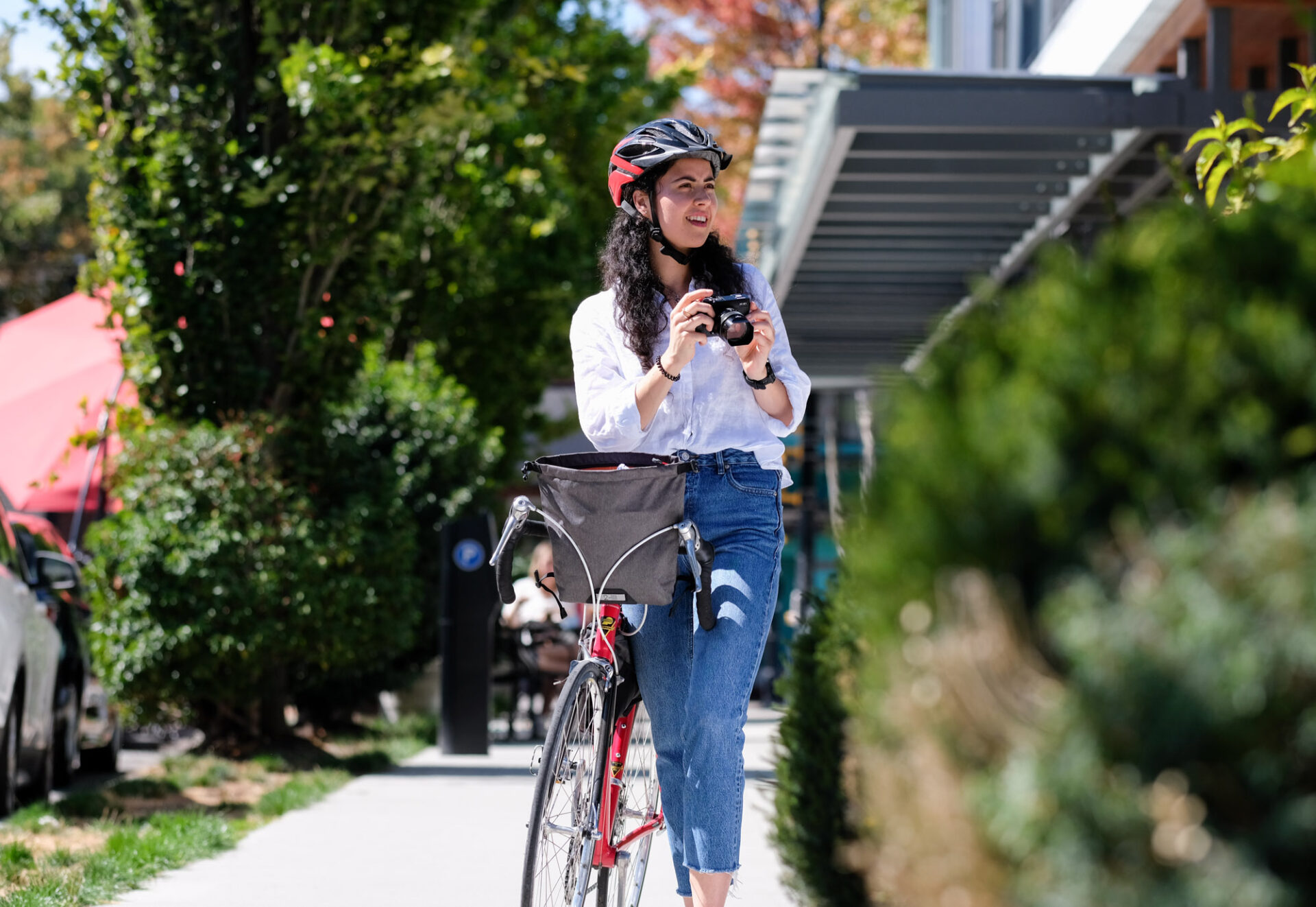 A woman composes a photo with her camera as she stands with her bike on a Vancouver street.