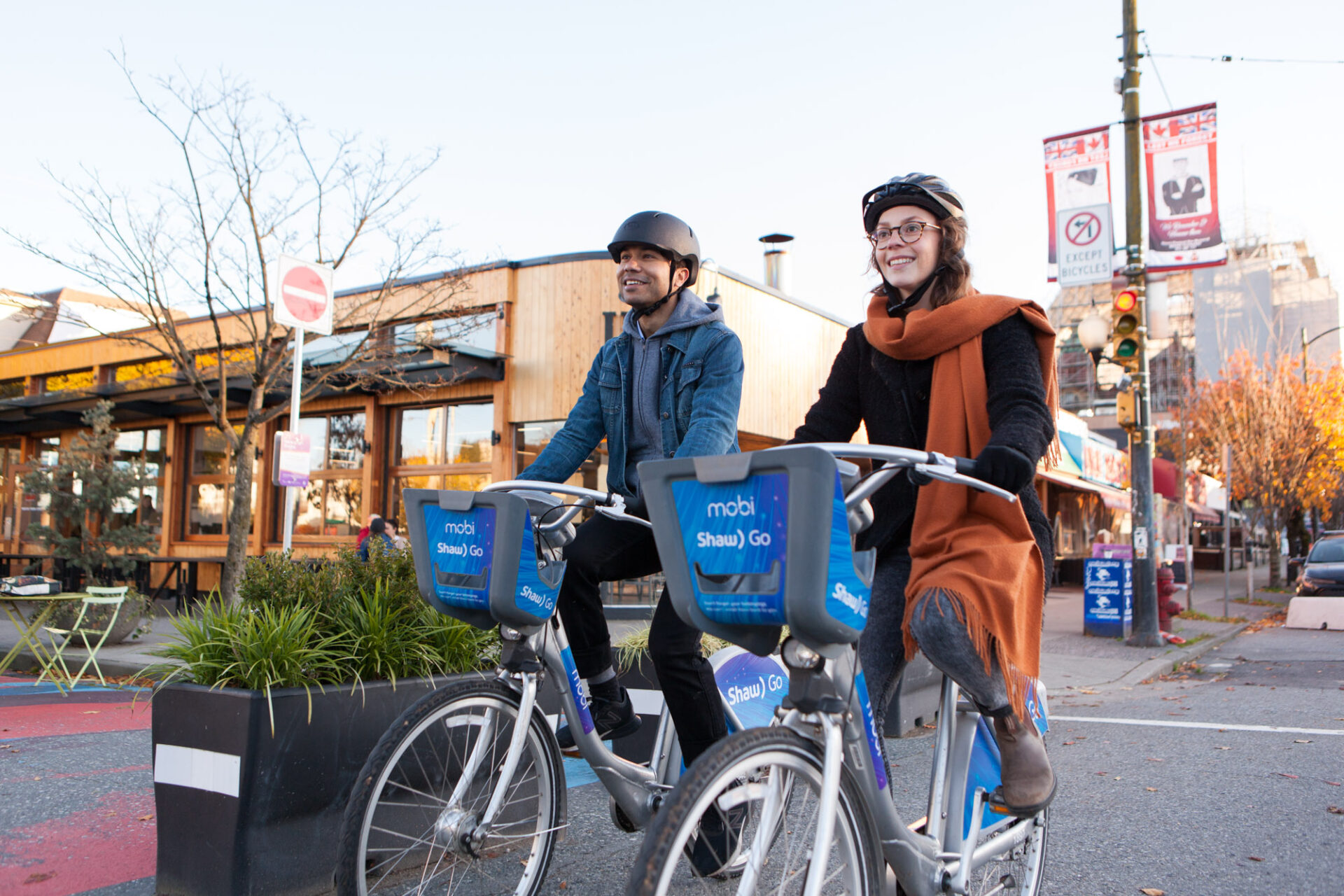 A man and woman ride bike share bicycles next to a coffee shop on Main Street, Vancouver.